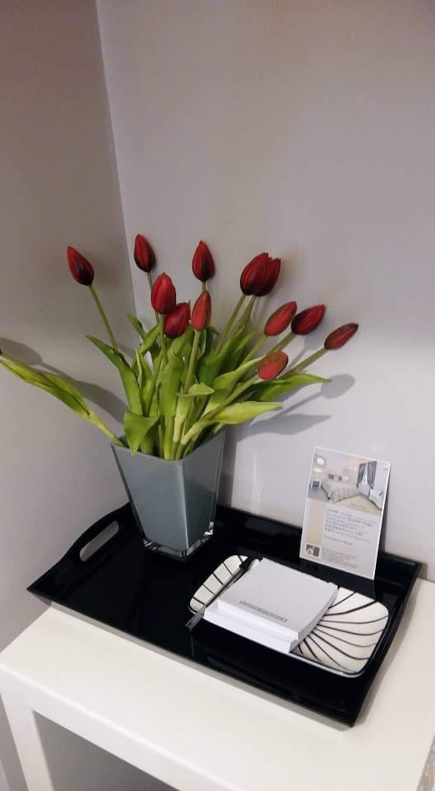 A white reception desk with a black tray holding a vase of red tulips and a brochure.
