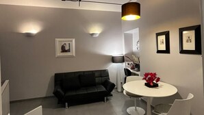 A modern living room with a black sofa, a round white table with chairs, and a ceiling light fixture. - ZUCCHELLI ROMAN RESIDENCE (Roma)