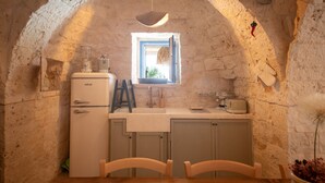 Eine kleine Küche mit Steinwand, einem Fenster, einem Kühlschrank, einer Spüle und einem Holztisch.