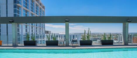 A rooftop pool with a clear view of the cityscape, surrounded by potted plants and seating areas.