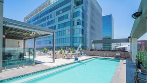 Un espace piscine aménagé sur le toit, doté d’une structure en verre, de chaises longues et offrant une vue sur un immeuble de grande hauteur.