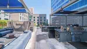 Une terrasse extérieure avec un espace barbecue, des sièges et une vue sur un bâtiment moderne.