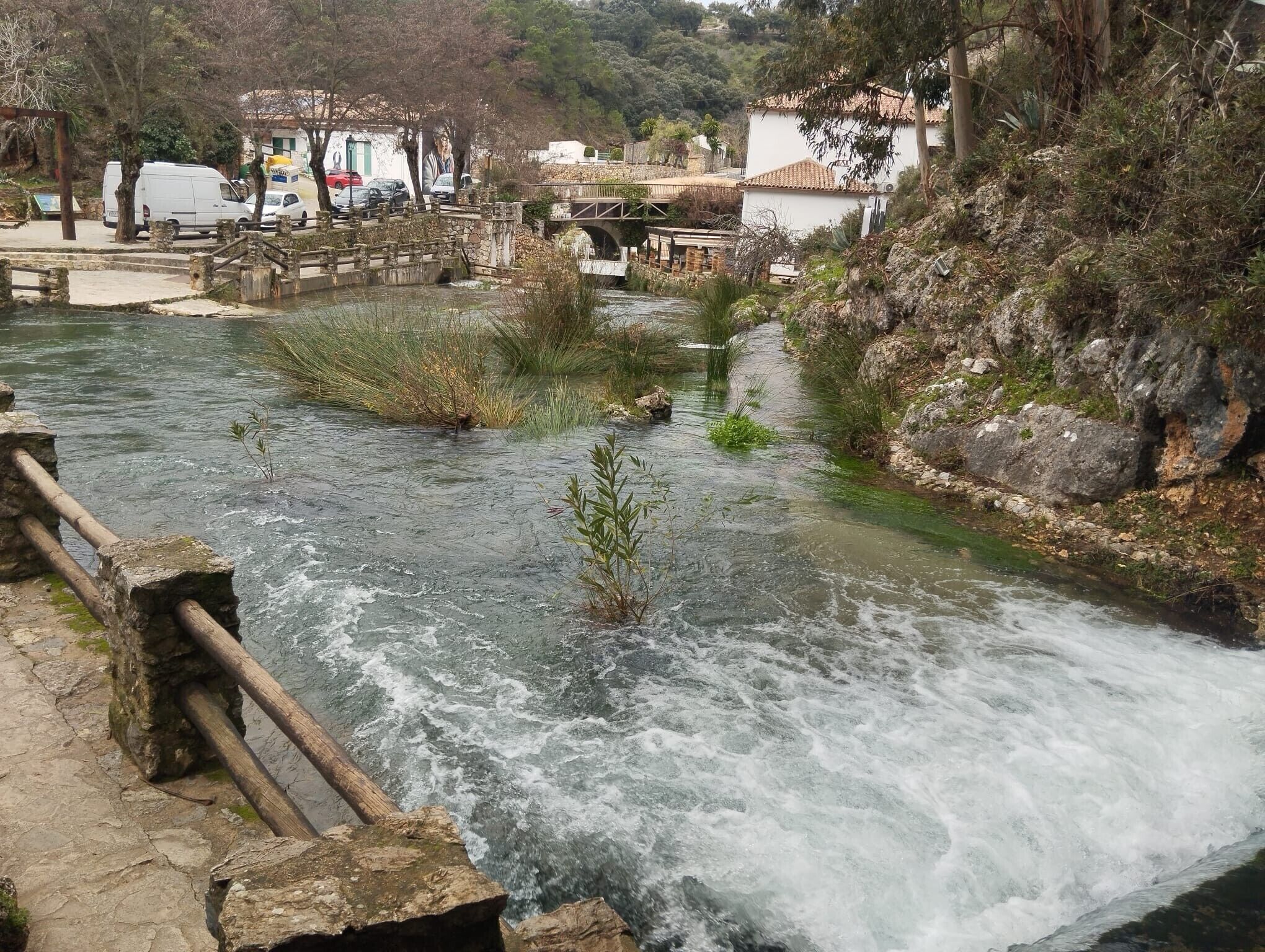 A river with a bridge, a stone pathway, and buildings in the background.