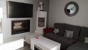 A modern living room with a flat-screen TV, fireplace, white coffee table, and a grey sofa with red cushions. - Holiday Home 'Alojamiento Patricia' with Mountain Views, Private Terrace and Wi-Fi (Igualeja)