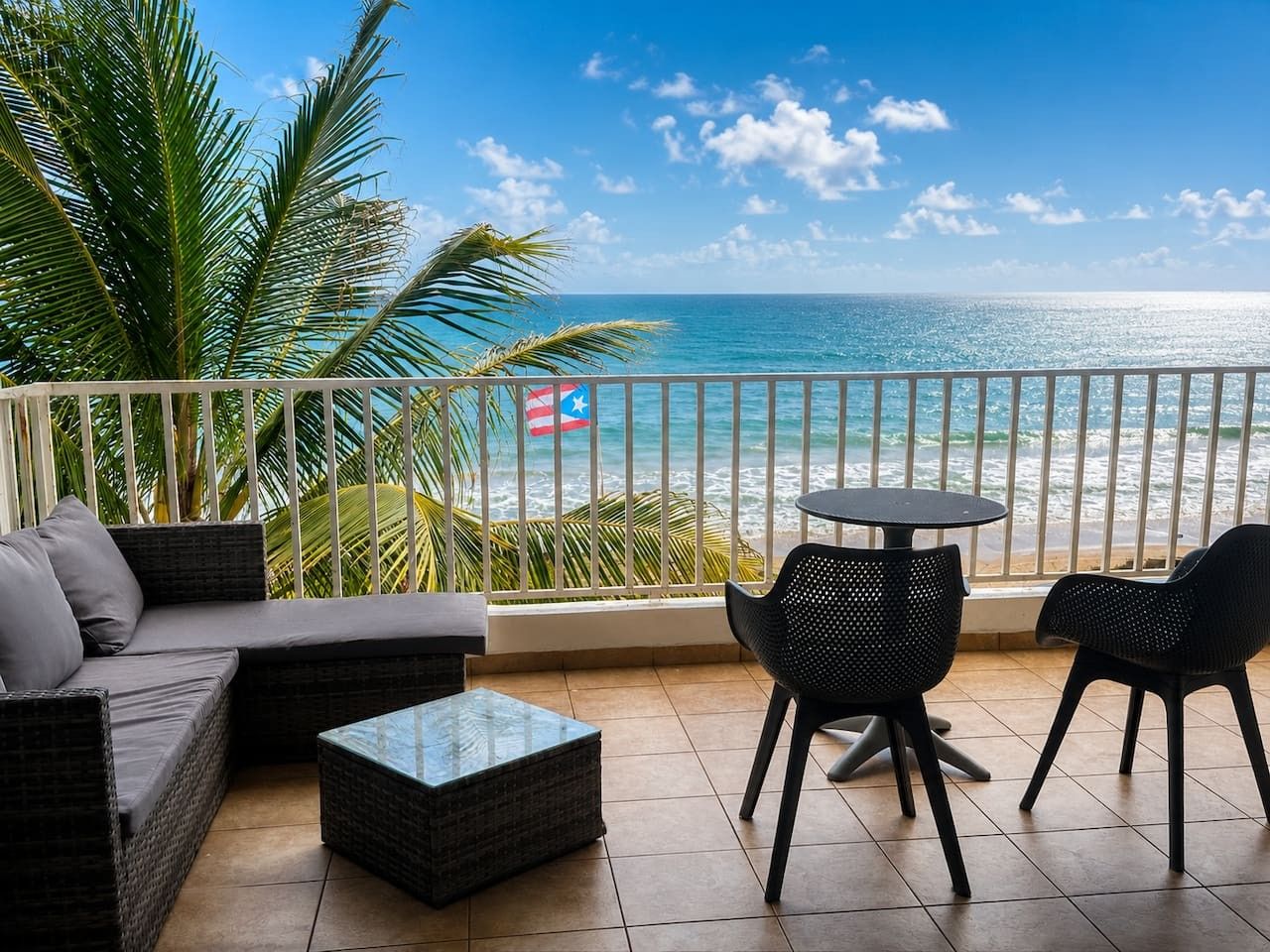 A balcony with a view of the ocean, a flag, and outdoor furniture.