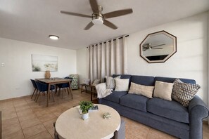 Ein Wohnzimmer mit einem dunkelblauen Sofa, einem runden Couchtisch und einem Essbereich mit einem Holztisch und blauen Stühlen.