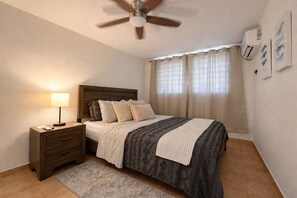 Ein Schlafzimmer mit einem Bett, einem Nachttisch, einer Lampe, einem Deckenventilator und Vorhängen.
