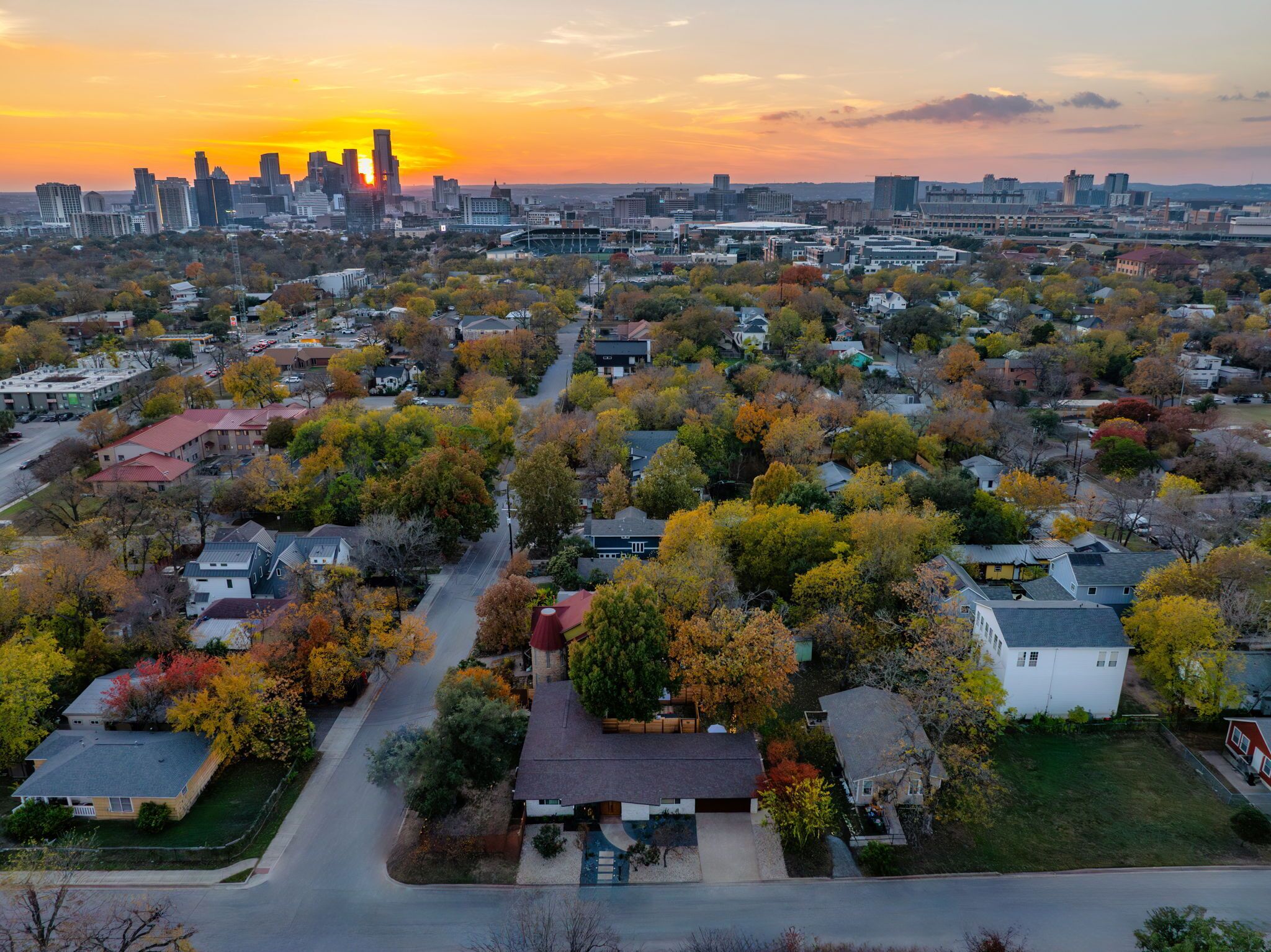 Luchtbeeld van een woongebied met huizen, wegen en een stadsachtergrond tijdens de zonsondergang.