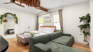 A modern bedroom with a bed, a green sofa, a mirror, and a potted plant. - Zen Den · Hot Tub · Cold Plunge · Movie Area (Austin)