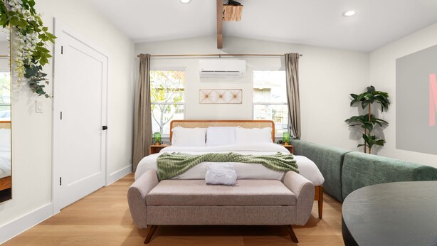 A modern bedroom with a bed, bedside tables, a green sofa, and a large window with curtains. - Zen Den · Hot Tub · Cold Plunge · Movie Area (Austin)