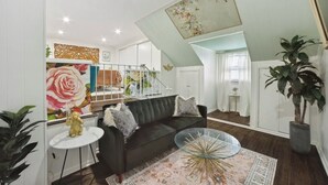 Een moderne woonkamer met een donkere bank, een glazen salontafel en een groot bloemen schilderij.