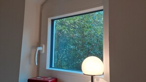 A window with a view of dense foliage, a white door, a red box, and a table lamp. - Relaxing time out on the Weser dyke (Bremen)