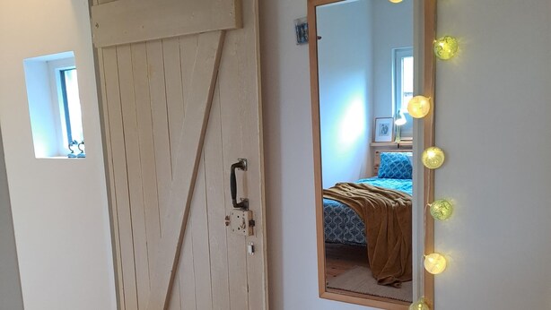 A room with a wooden door, a mirror with lights, and a bed with a blue blanket. - Relaxing time out on the Weser dyke (Bremen)