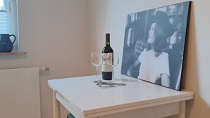 A small, white table with a bottle of wine and two glasses on it, a black and white photograph on the wall, and a green stool. - Relaxing time out on the Weser dyke (Bremen)