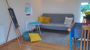 A living room with a grey sofa, yellow cushions, a small table, and an easel with a painting. - Relaxing time out on the Weser dyke (Bremen)