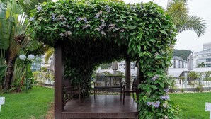 A wooden pergola with a bench, surrounded by lush greenery and flowers. - Apto c/ Churrasqueira a 400m da Praia MDR0104 (Florianópolis)