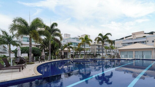 A swimming pool with lounge chairs and palm trees, surrounded by modern buildings. - Apto c/ Churrasqueira a 400m da Praia MDR0104 (Florianópolis)