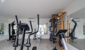 A gym with exercise equipment, a mirrored wall, and a view of the outside. - Apto c/ Churrasqueira a 400m da Praia MDR0104 (Florianópolis)