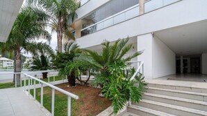 A modern building with a staircase, palm trees, and a white railing. - Apto c/ Churrasqueira a 400m da Praia MDR0104 (Florianópolis)