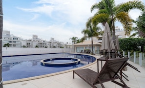 A rooftop swimming pool with lounge chairs and umbrellas, surrounded by palm trees and modern buildings. - Apto c/ Churrasqueira a 400m da Praia MDR0104 (Florianópolis)