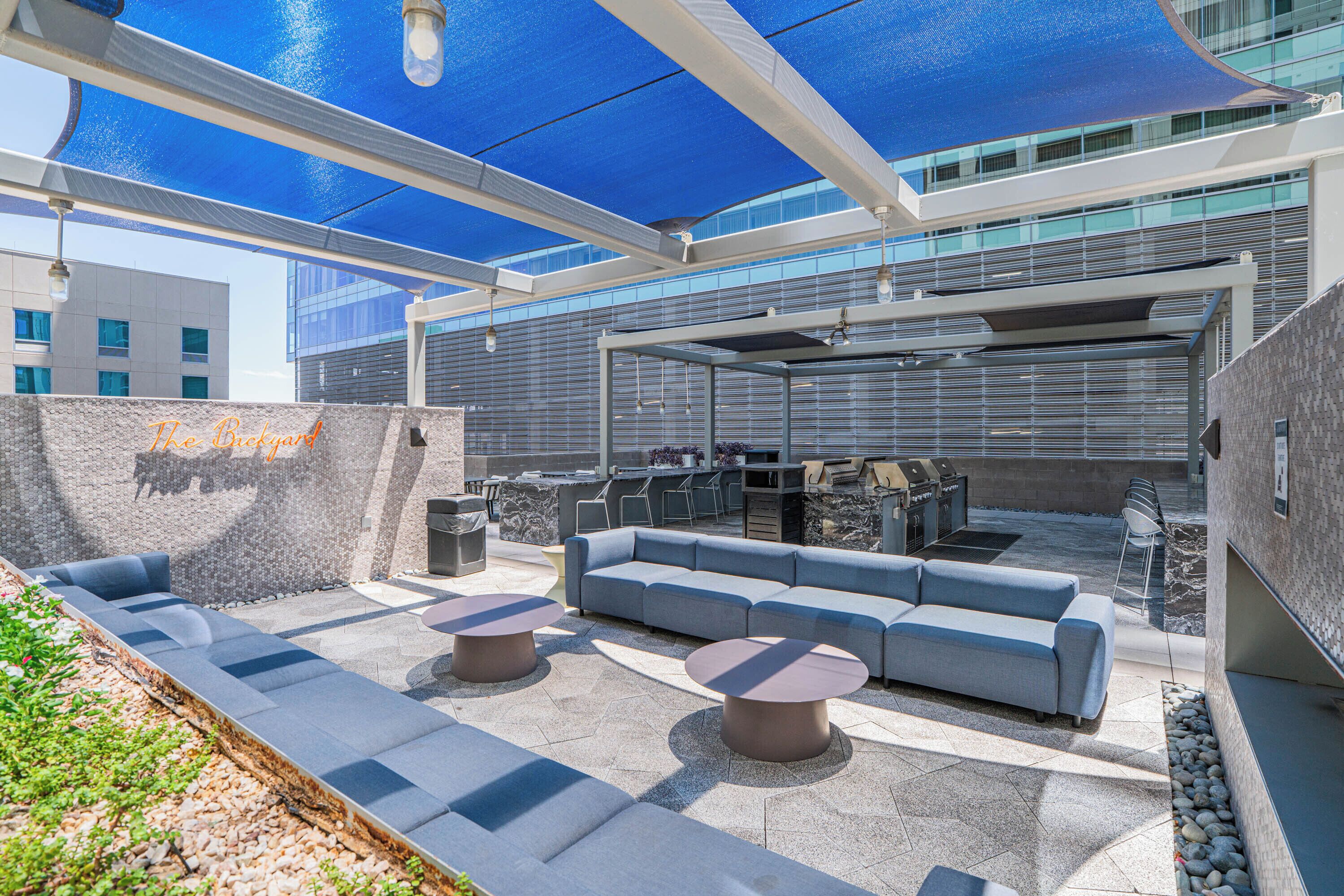 An outdoor patio area with a blue canopy, seating arrangements, and a barbecue setup.