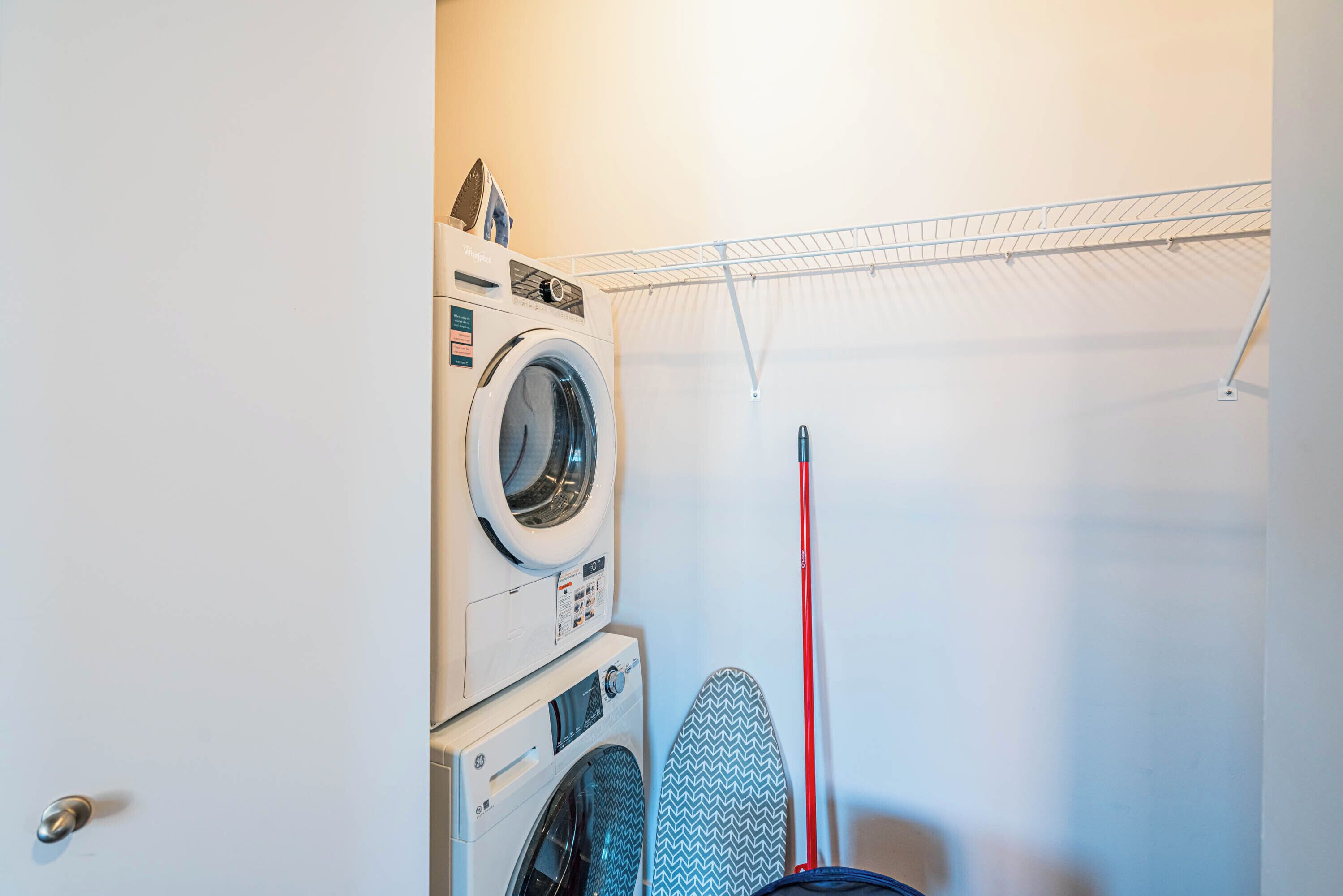 Un espace buanderie équipé d’une pile de machines à laver et de sèche-linge, d’un étendoir et de planches à repasser.