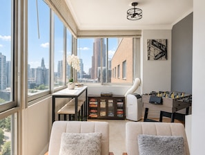 A modern living room with large windows, a sofa set, a foosball table, and a small table with a potted plant. - The ATL Sky Suite High-Floor 3BR Downtown Penthouse Stunning City Views (Atlanta)