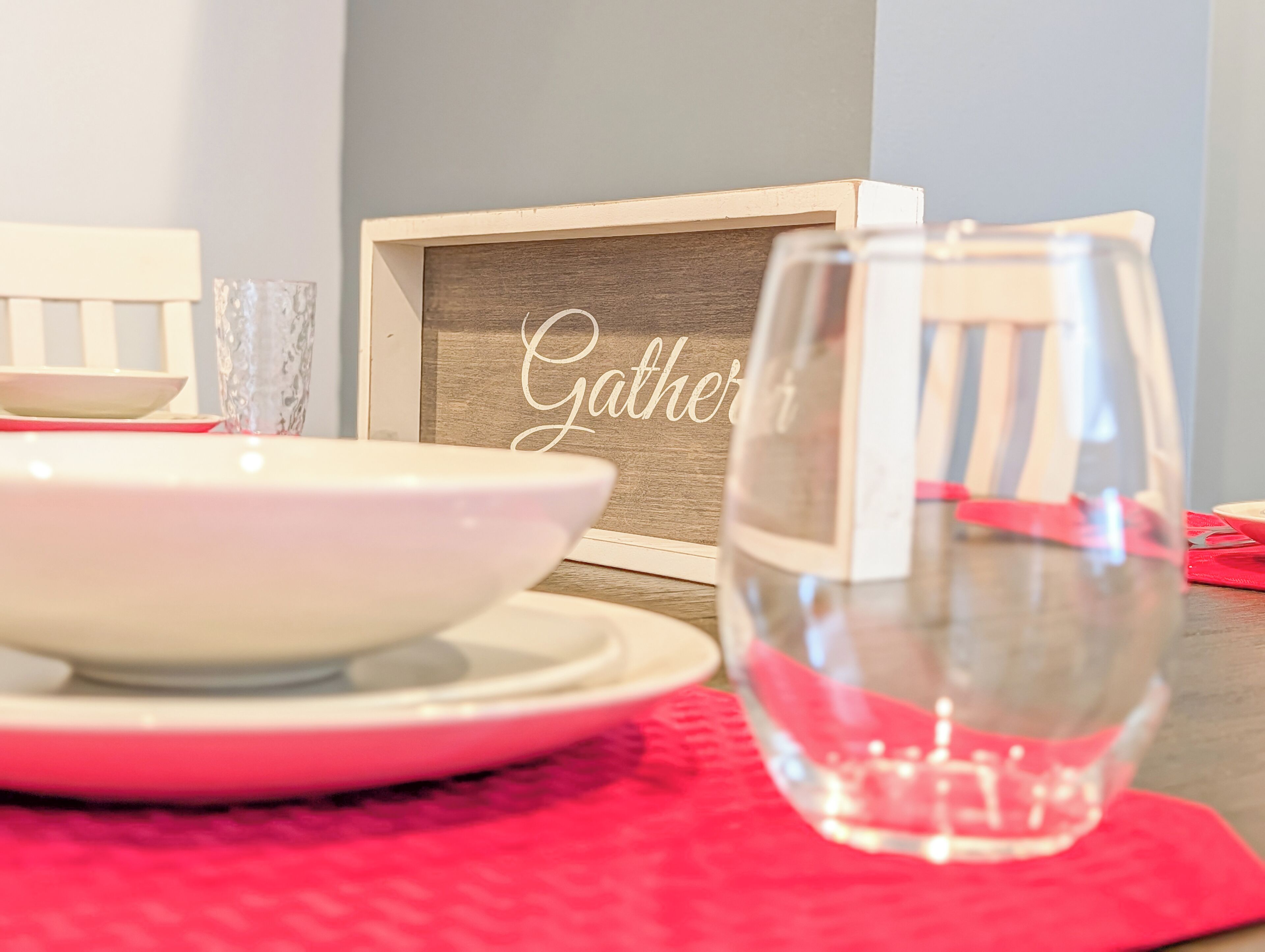 A dining setup with a bowl, a glass, and a framed sign with the word 'Gather'.