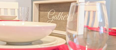A dining setup with a bowl, a glass, and a framed sign with the word 'Gather'.