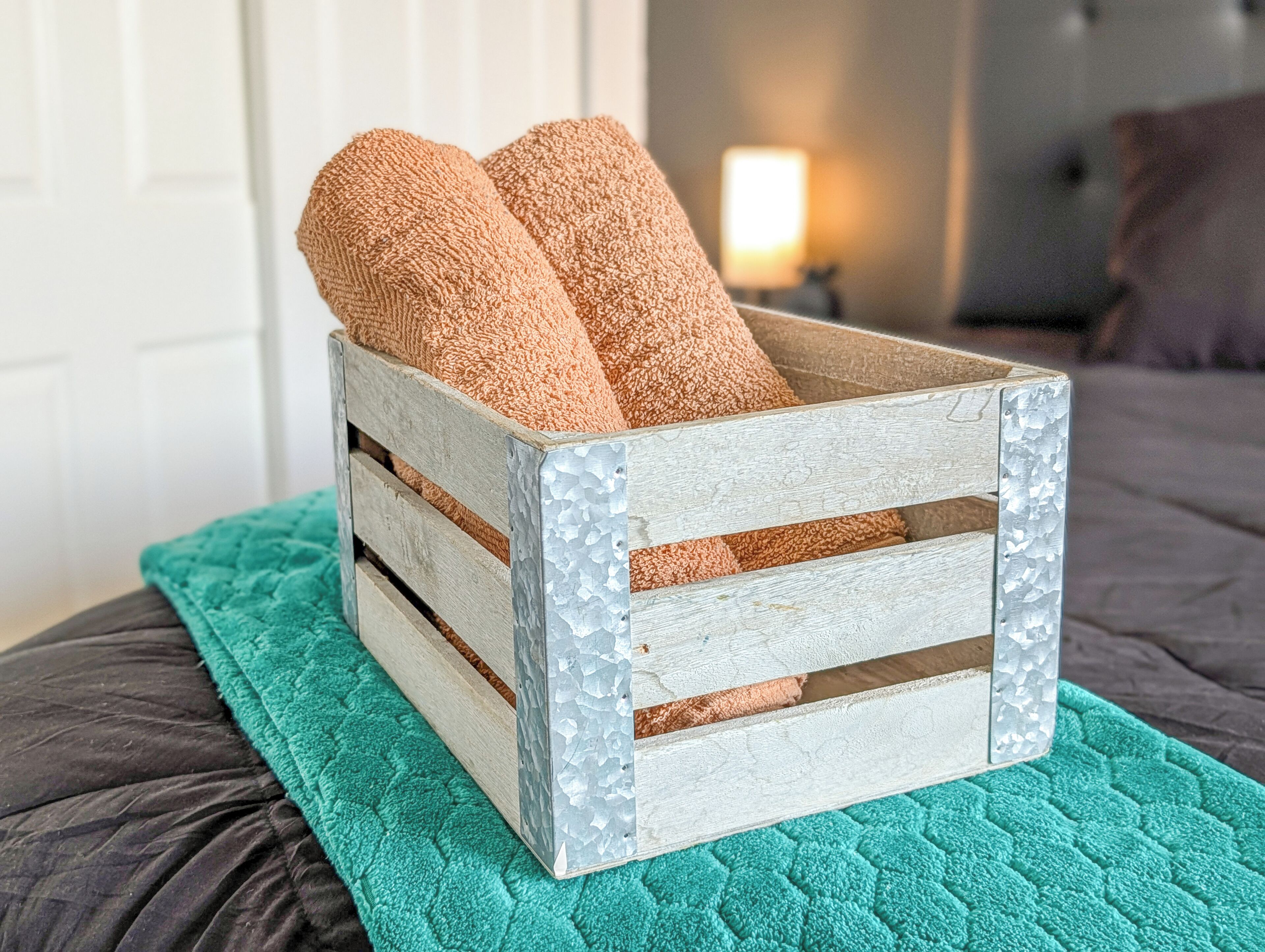 Una caja de madera rústica con dos toallas sobre un edredón color turquesa.