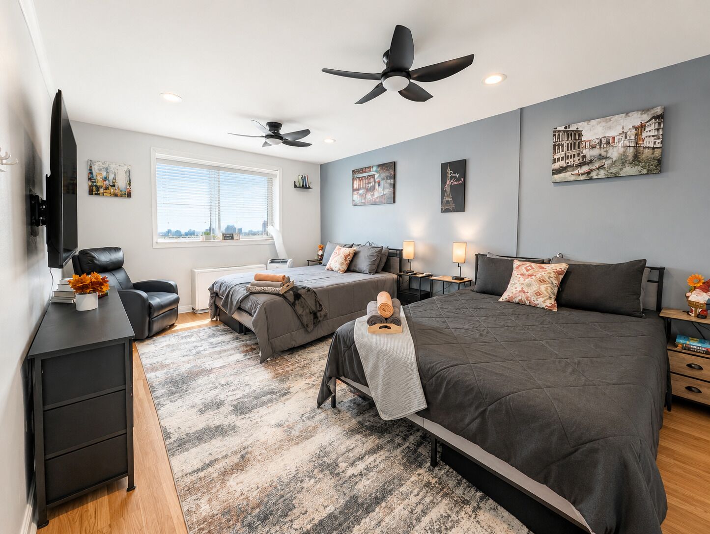 A modern bedroom with a large bed, two smaller beds, a desk, and a ceiling fan.