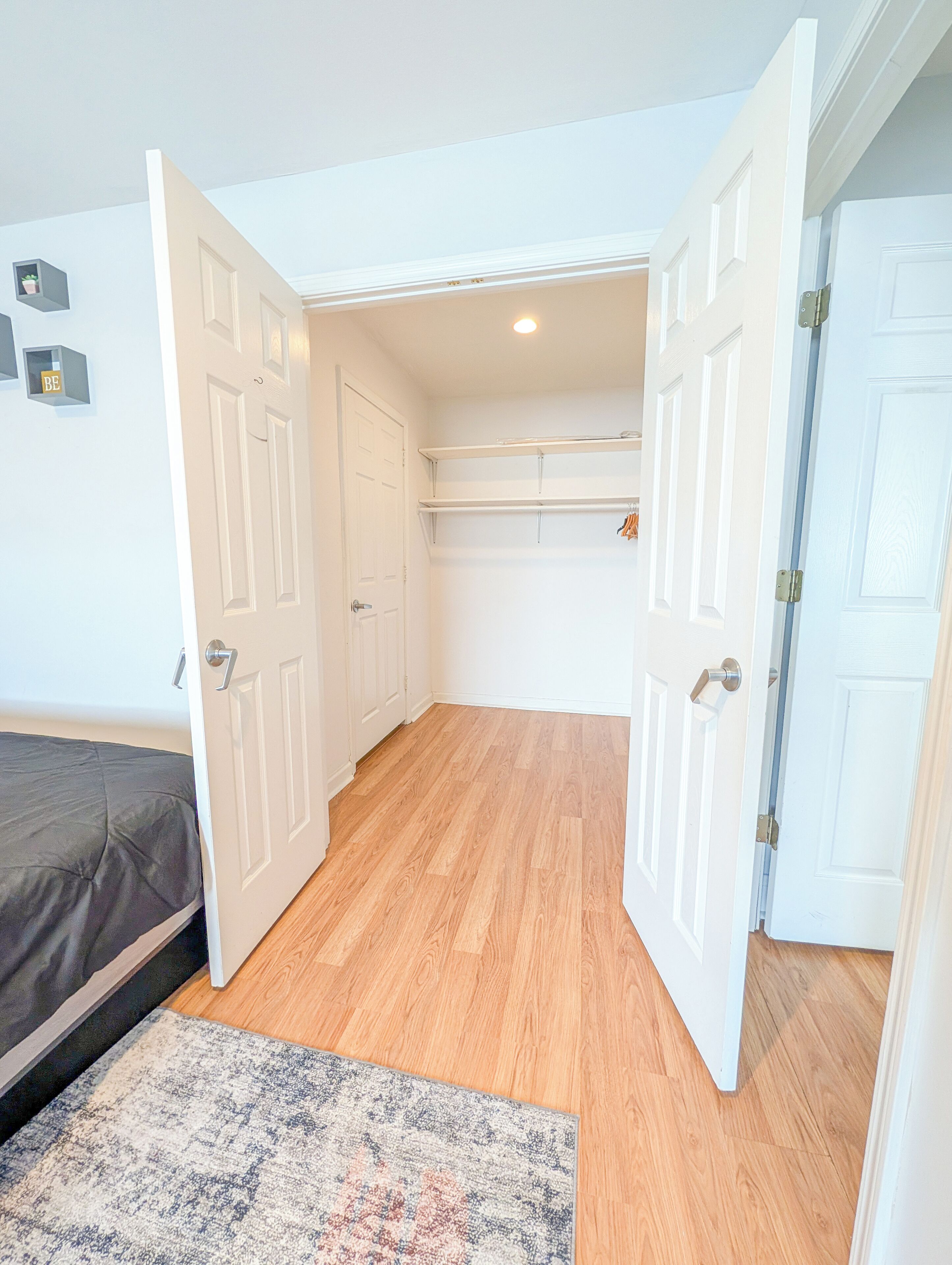 Een slaapkamer met een bed, vloerkleed en een kledingkast met hangende kleding.