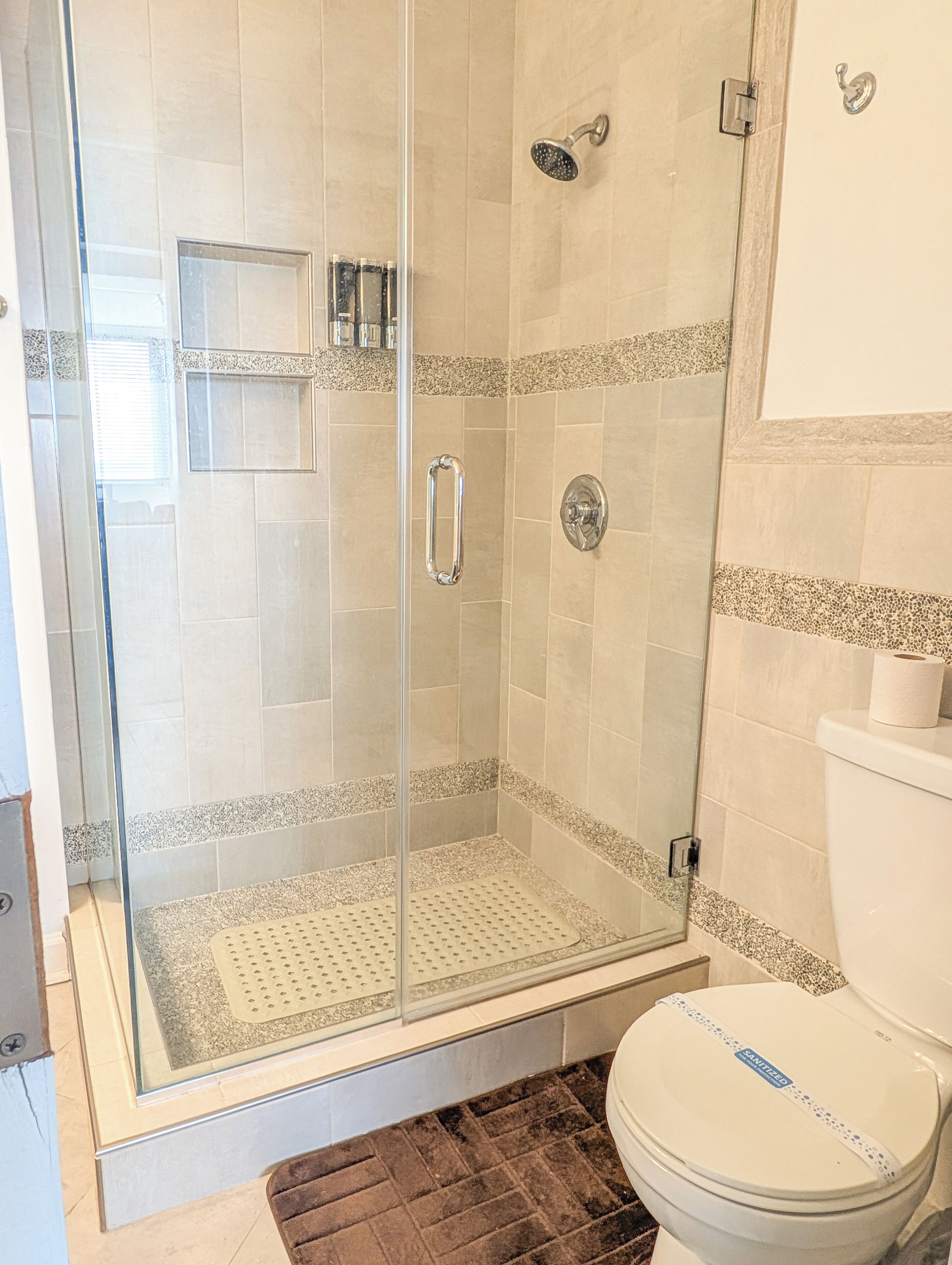 A shower with a glass door, a toilet with a 'SANITIZED' label, and a tiled floor.