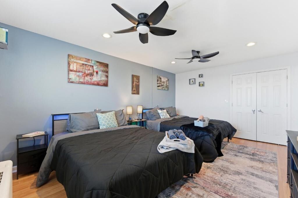 A modern hotel room with two beds, a ceiling fan, artwork on the walls, and a large wardrobe.