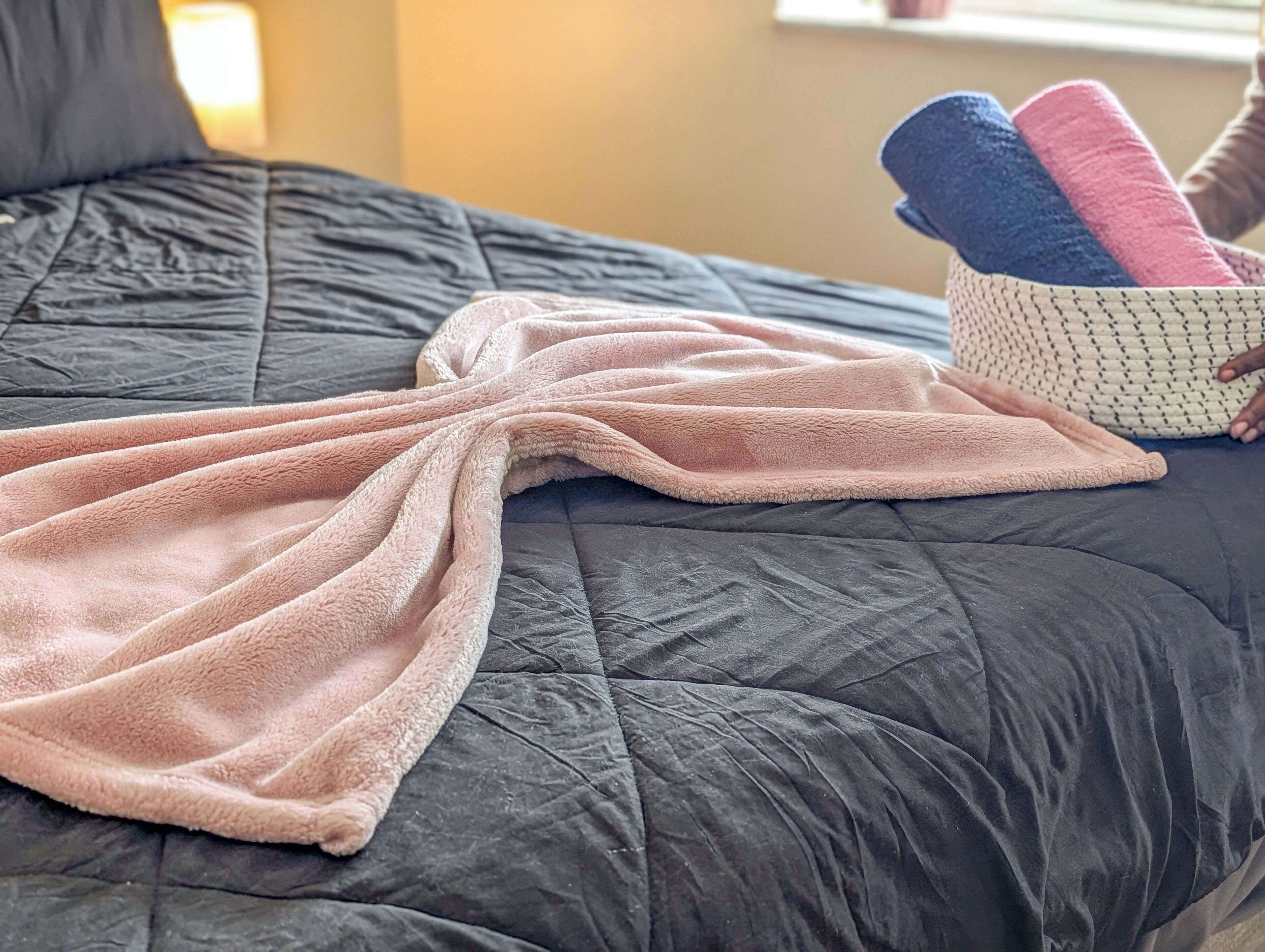 Una cama con un edredón oscuro y una manta rosa.
