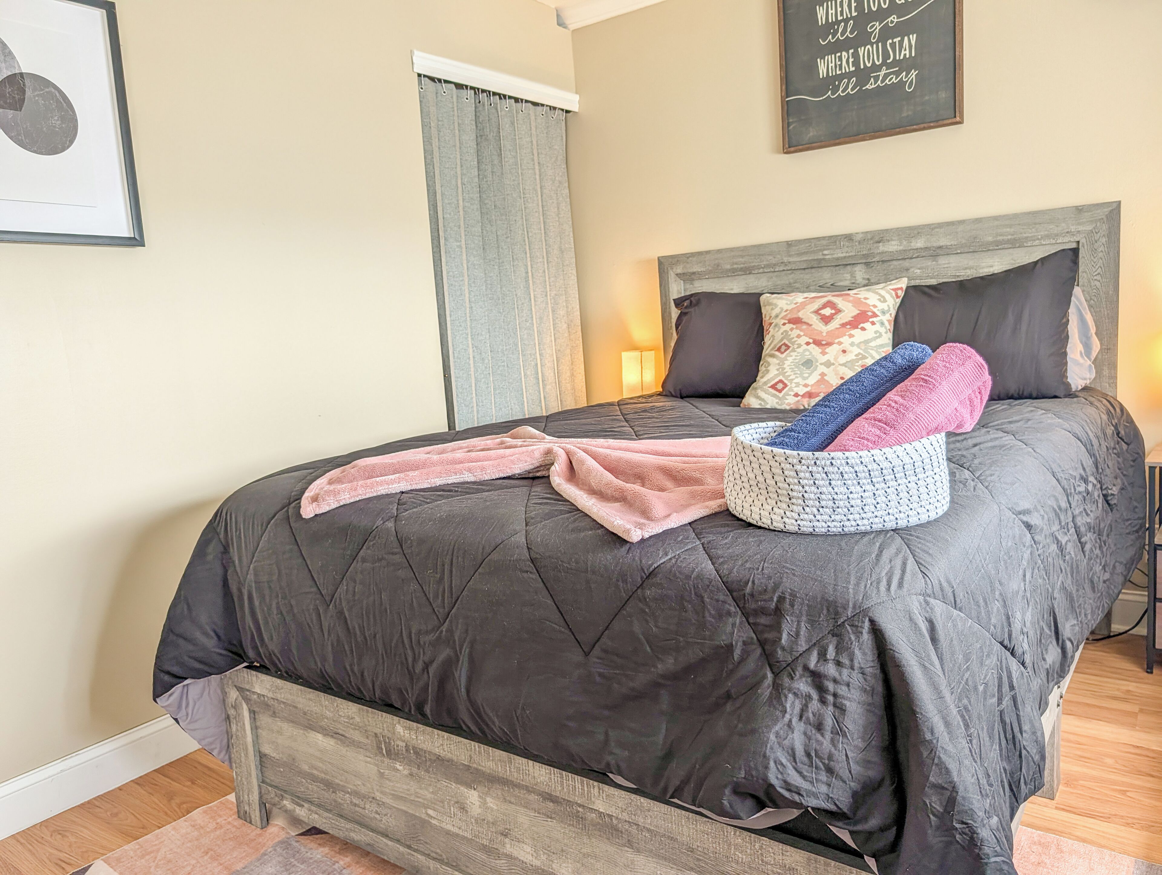 A bed with a dark quilt, a pink towel, and a knitted basket.