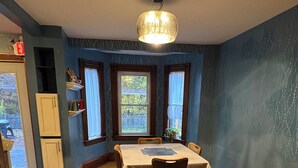Un comedor con piso de madera en espiga, una mesa redonda con sillas, una araña y ventanas con cortinas.