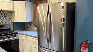 Una cocina con armarios blancos, un refrigerador de acero inoxidable, una estufa a gas y una pared azul.