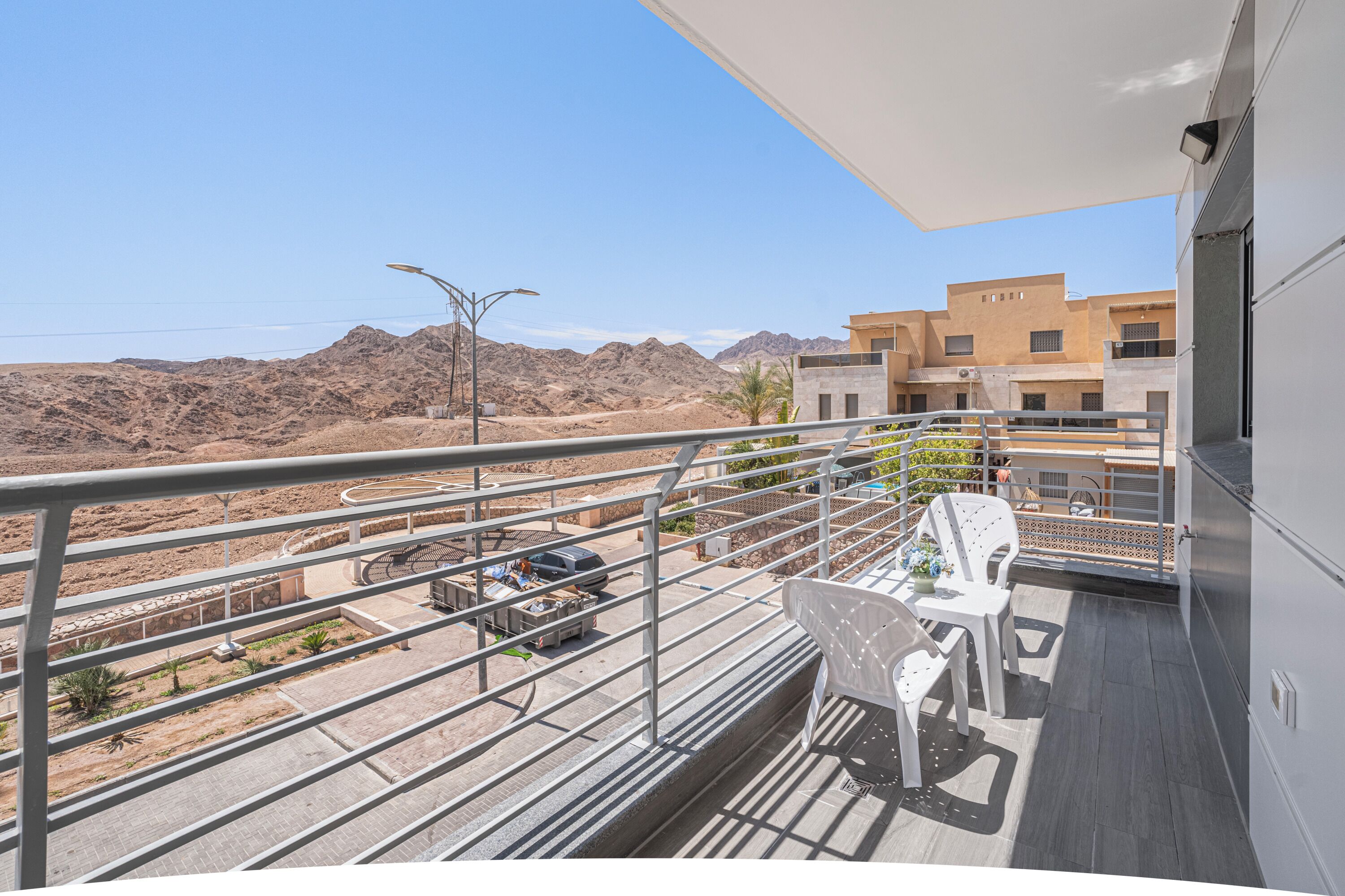 Uma varanda com vista para uma paisagem desértica, mesa e cadeiras, e um edifício com design moderno.