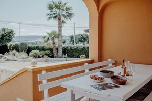 Taula blanca preparada amb ampolla, gots, bols i menú a un balcó que ofereix vista a palmeres i una tanca.