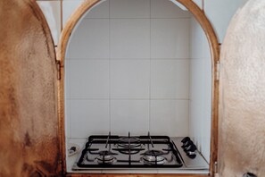 A kitchen with a gas stove, white tiled backsplash, and wooden arch framing the space. - Villa Carla al Capitolo (Monopoli)