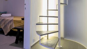 Een kamer met een wenteltrap, een bed met dekbed en een hoed aan de muur.