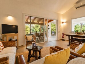 A living room with a television, wicker furniture, a coffee table, and a sliding glass door leading to an outdoor patio. - Villa Claudia Relax & Garden – Torre delle Stelle (Torre Delle Stelle (Maracalagonis))
