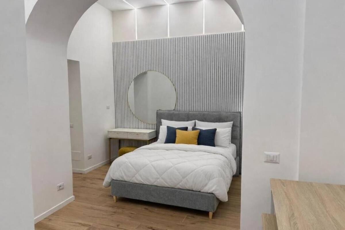 Une chambre à coucher avec un lit, une table de chevet, un miroir et un mur orné de lignes verticales.