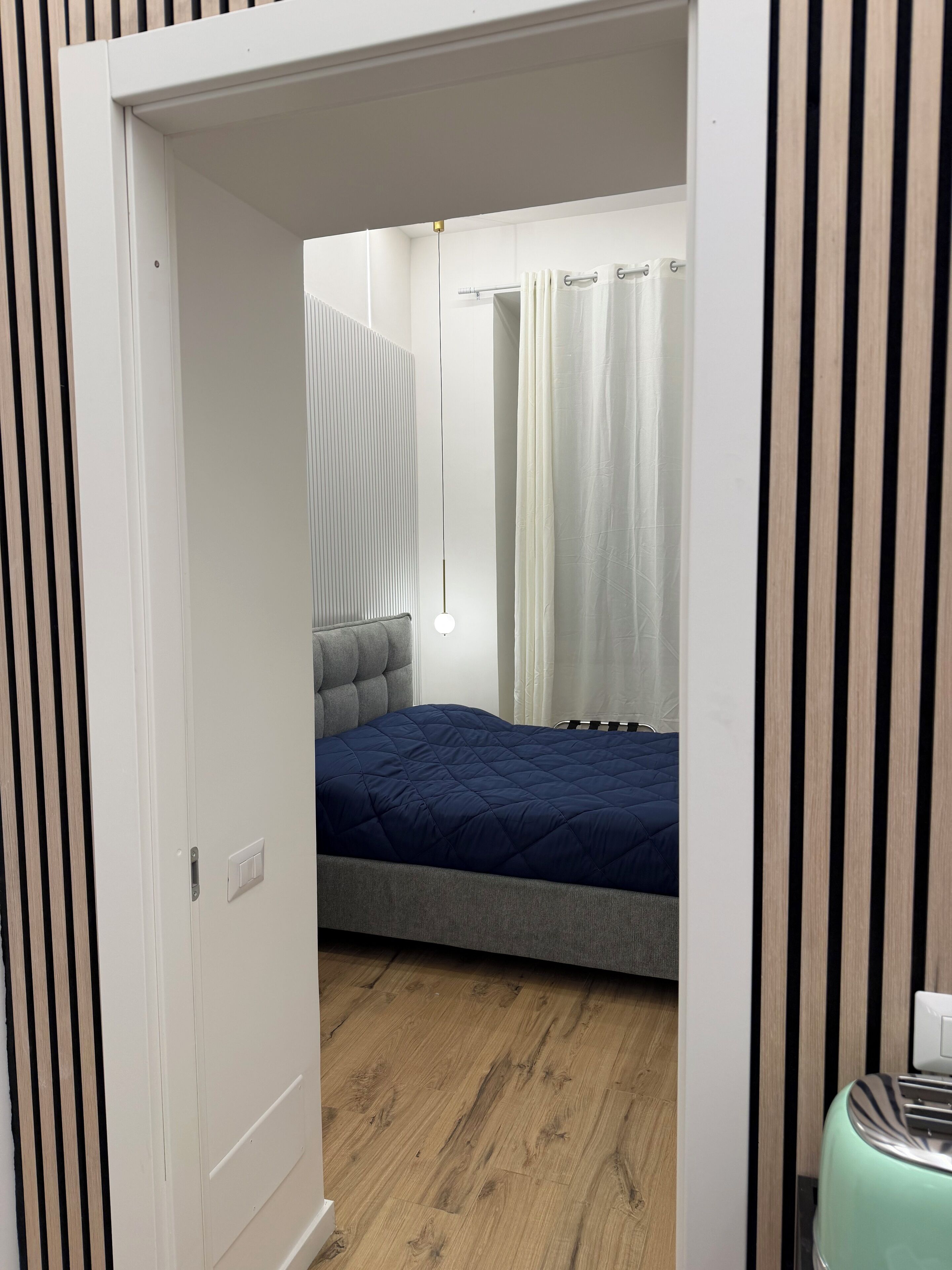 A bedroom with a bed, a bedside table, a hanging light, and a window with curtains.