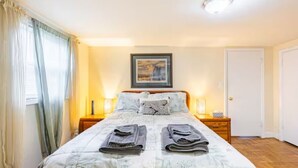 A neatly made bed with folded towels, a framed picture on the wall, and a door to the right. - Ground floor apartment 10 mi from D.C. and still feels like countryside! (Bethesda)