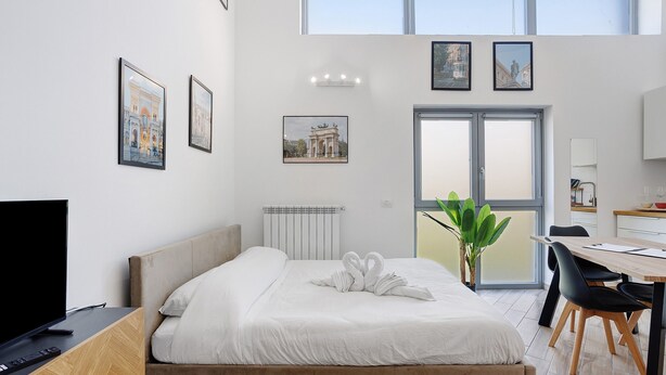 Habitación de hotel moderna con cama, televisor, zona de comedor y obras de arte en las paredes.