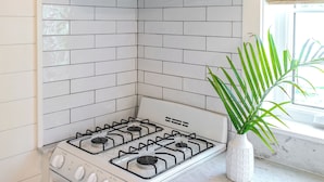 A kitchen with a white stove, a backsplash with white and gray tiles, and a plant on the counter.