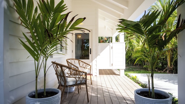 A covered outdoor area with two potted plants, a wicker chair, and a white cabinet.