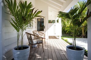 A covered outdoor area with two potted plants, a wicker chair, and a white cabinet.